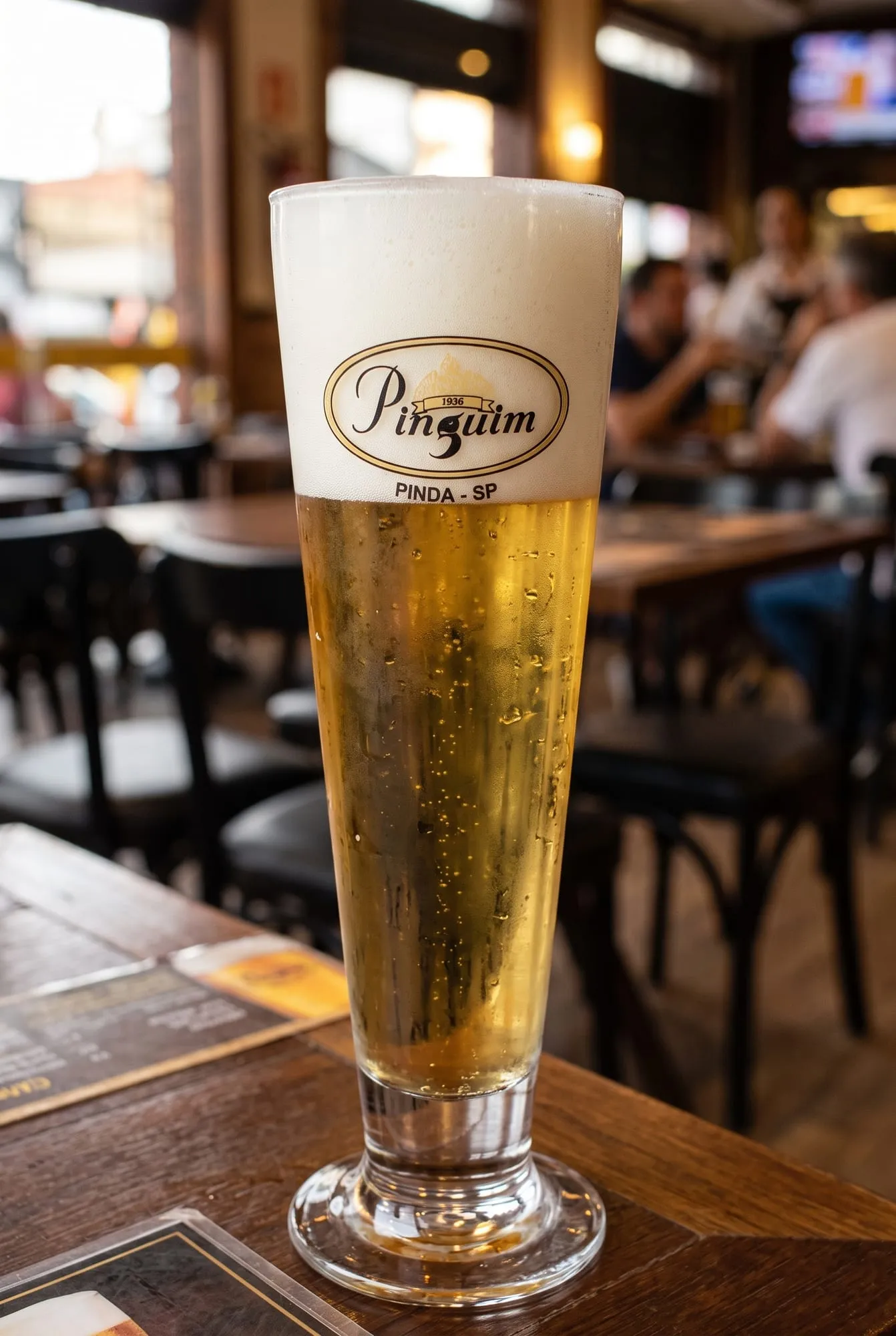 Tulipa de chopp Pinguim com o colarinho de creme, sobre a mesa do salão